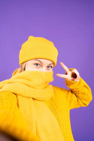 紫の背景に隔離されたスカーフで顔を覆う冬服の女性のセルフィー — ストック写真