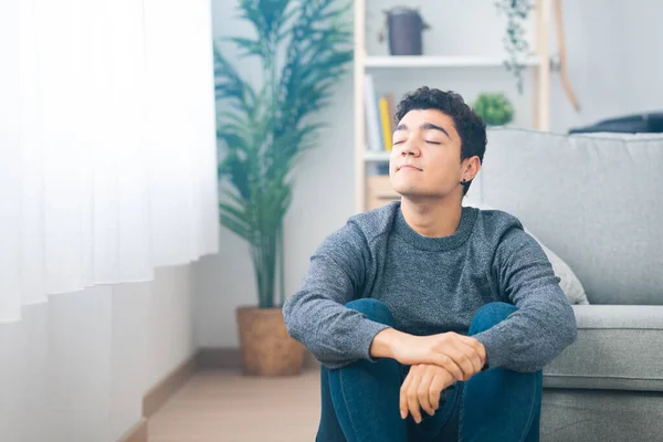 Hispanic teenager boy inhaling while sitting on floor at home