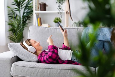 Young woman having video call on phone while lying on back on couch.