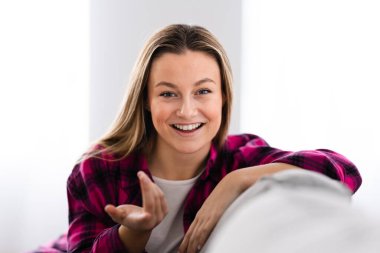 Pretty cheerful woman talking and looking to camera sitting on sofa.