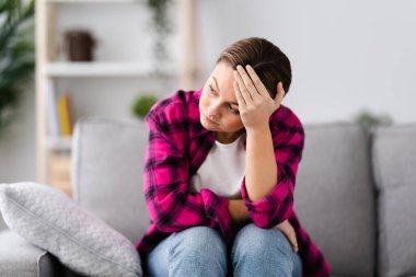 Sad young woman suffering depression hand on head sitting on couch. Anxiety and mental health concept