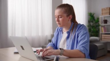 Young woman working on laptop, then checking her smartwatch and writing on notebook