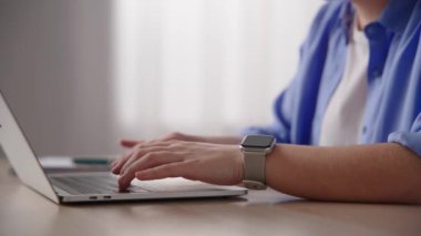 Closeup of hands typing on laptop, then checking smartwatch.