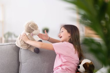 Kid sitting on sofa and talking to fluffy toy