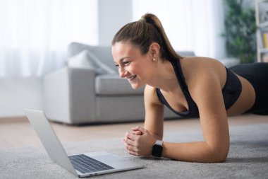 Happy fit woman working out at home following fitness video tutorial. Sportswoman making a plank