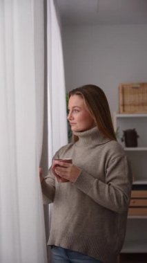 Young woman looking from the window and drinking coffee or tea