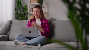 Young woman having video conference on laptop while sitting on couch in the living room. Person talking to webcam