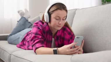 Young woman lying down on sofa and having video call on telephone.