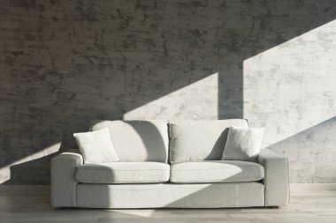 Sofa in front of cement wall illuminated by sunlight with window shapes
