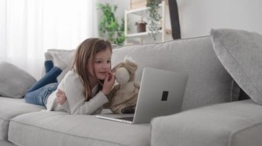 Bilgisayarında video kaydı olan bir çocuk. Küçük kız kanepede uzanıyor..