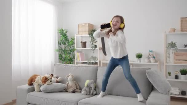 活泼的小女孩在沙发上跳啊跳啊跳 小孩在公寓里听音乐 — 图库视频影像