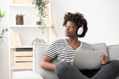 Evde dizüstü bilgisayarla çalışırken düşünen Afrikalı Amerikalı bir kadın..