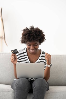 Mutlu Afro-Amerikan genç bayan laptopun önünde online alışveriş yapıyor..