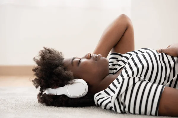 African American woman listening to music on headphones while lying on the floor.