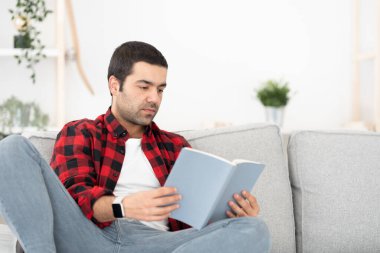 Kanepede oturup kitap okuyan İspanyol genç adam. Evde öğrenim görüyorum..
