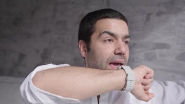 Kanepede oturmuş, akıllı saatle konuşan İspanyol genç adam.