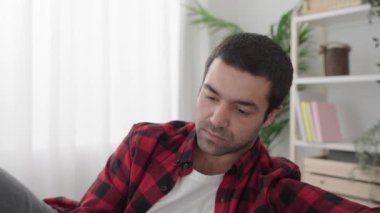 İspanyol genç adam oturma odasındaki kanepede kitap okuyor.