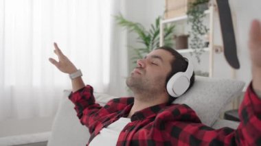 Kanepede otururken kulaklıkla müzik dinleyen İspanyol genç adam.