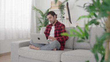 İspanyol adam laptopta sohbet ediyor. Genç adam canlı yayında evdeki kanepede oturuyor.