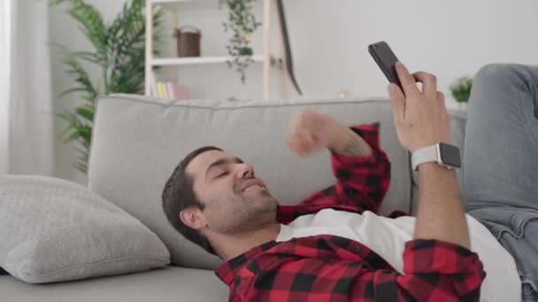 西班牙裔年轻人一边打电话一边在公寓沙发上休息 — 图库视频影像