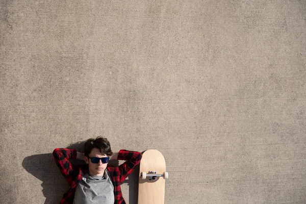 少年放松地躺在滑板旁边的水泥地板上 复制空间的背景 — 图库照片