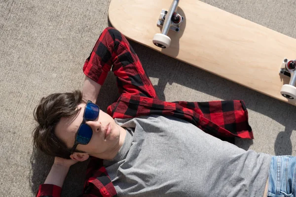 スケートボードの横に床に横たわっティーンエイジャーのスケーター男の子のトップビュー — ストック写真