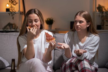 Arkadaşları geceleri onu uyarırken güzel bir kadın yemek yiyor. Pijama giyen kız kardeşler pizza yiyorlar.