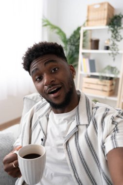 Bir fincan kahve içerken selfie çeken Afrikalı Amerikalı genç bir adam. Siyah adam kameraya konuşuyor..