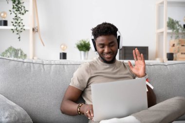 Genç Afro-Amerikalı adam kanepede otururken dizüstü bilgisayarında video görüşmesi yapıyor..