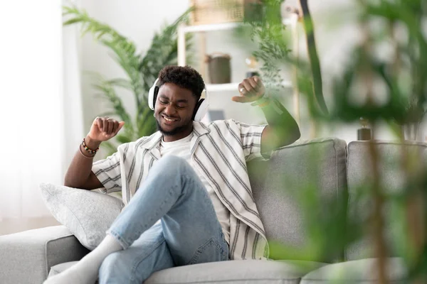 stock image Black young man listening to music and dancing on sofa.