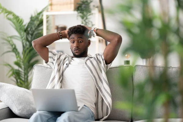Worried black young man looking at laptop. Working from home concept.