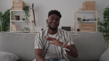 Afrikalı Amerikalı genç bir adam bir dairede kanepede otururken kamerayla konuşuyor. Siyah kişi canlı yayında ya da video çağrısı alıyor