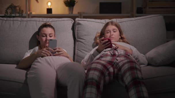 Dua Wanita Muda Berbaring Sofa Berkonsentrasi Pada Ponsel Saudara Perempuan — Stok Video