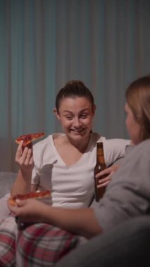 Geceleri pizza yerken kanepede sohbet eden iki genç kadın. Arkadaşlar konuşuyor ve dedikodu yapıyorlar..