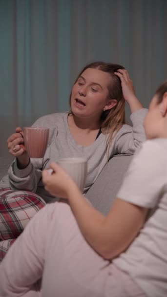 年轻女人在沙发上和最好的朋友聊天 姐妹俩晚上一起喝咖啡 在家里谈话的女同性恋夫妇 — 图库视频影像