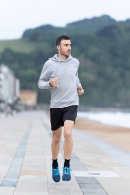 Genç yetişkin bir adam dışarıda koşuyor. Kapüşonlu spor antrenmanı.
