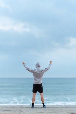 Adam ufka bakıyor ve ellerini kaldırıyor. Sporcunun başarısını kutlayan arka görünümü.