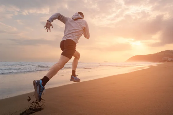 Güneşin doğuşunda ya da batışında plajda hızla koşan sporcunun arka görüntüsü. Açık havada fotokopi alanı olan bir sporcu. Spor motivasyonu kavramı