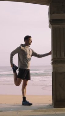 Genç sporcu dışarıda bacaklarını açıyor. Koşucu antrenmandan önce ısınıyor