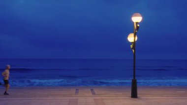 Geceleri sahilde koşan bir sporcu, plajın yanında. Koşucu egzersiz yapıyor