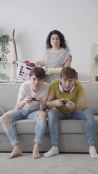 10代の息子がビデオゲームをして彼女を無視している間に怒っている母親の叱り 男の子に服を投げる女性 平等の概念 — ストック動画