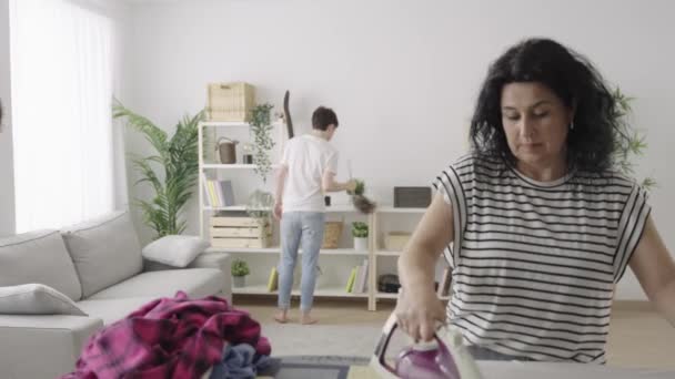 家族が一緒に家を掃除します 母親のアイロンと息子は家事をする １０代の男の子が家で助けている 平等の概念 — ストック動画