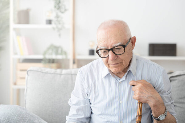Sad elderly man sitting on sofa. Depression and loneliness concept