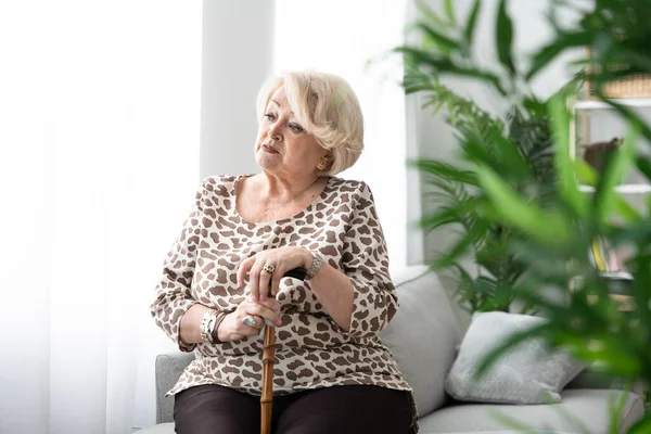Elderly woman thinking supported on walking stick