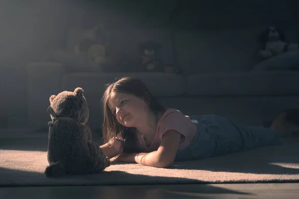 stock image Little girl looking at soft toy and playing in the living room with sunset light.