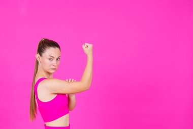 Pembe arka planda izole edilmiş, yumruğu havada güçlü genç bir kadın..