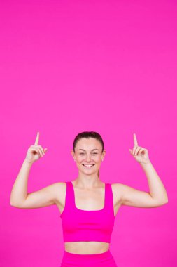 Gülümseyen sporcu kadın pembe fotokopi alanını işaret ediyor. Genç bir kadın kameraya bakıyor ve mesaj gösteriyor.