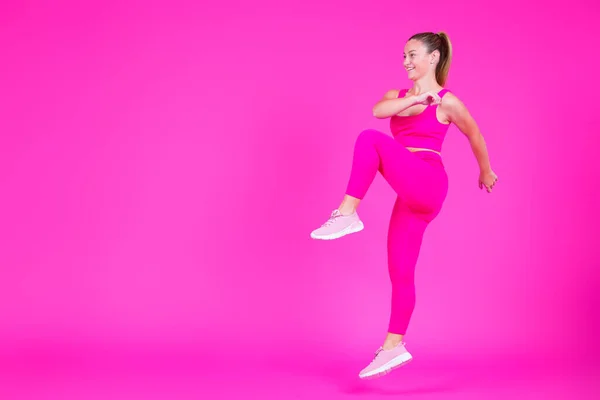 stock image Full length of young woman doing exercise isolated on pink background with copy space. Sportswoman jumping.