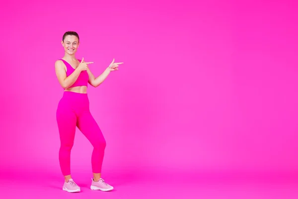 全长的女运动员指着粉红色的复制空间 健身教练在生机勃勃的背景下展示孤立的信息 — 图库照片