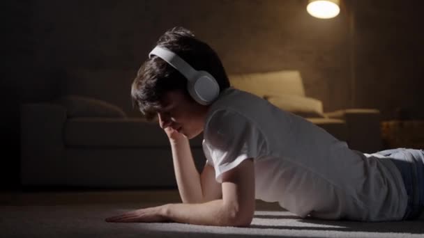 Θετικό Έφηβο Αγόρι Που Ακούει Μουσική Ακουστικά Και Χορεύει Ξαπλωμένος — Αρχείο Βίντεο